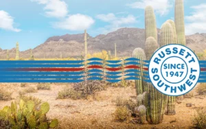 Desert landscape with cacti and mountains under a blue sky, overlaid with a blue and red wavy stripe and a circular Russett Southwest Since 1947 logo.